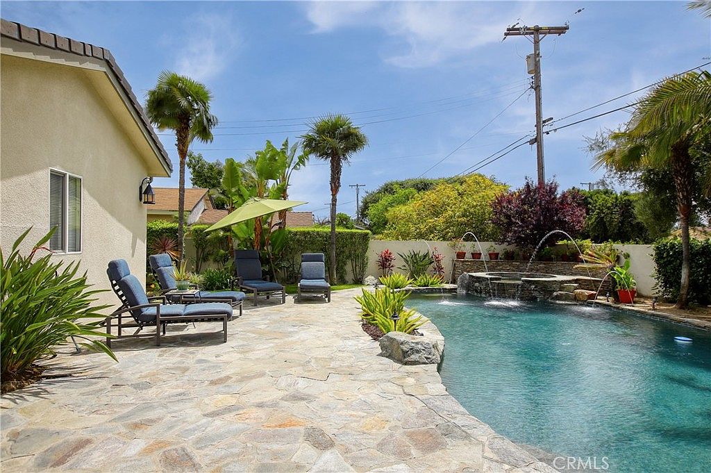 The pool seen from the stone deck, with water-feature jets and a planted privacy hedge