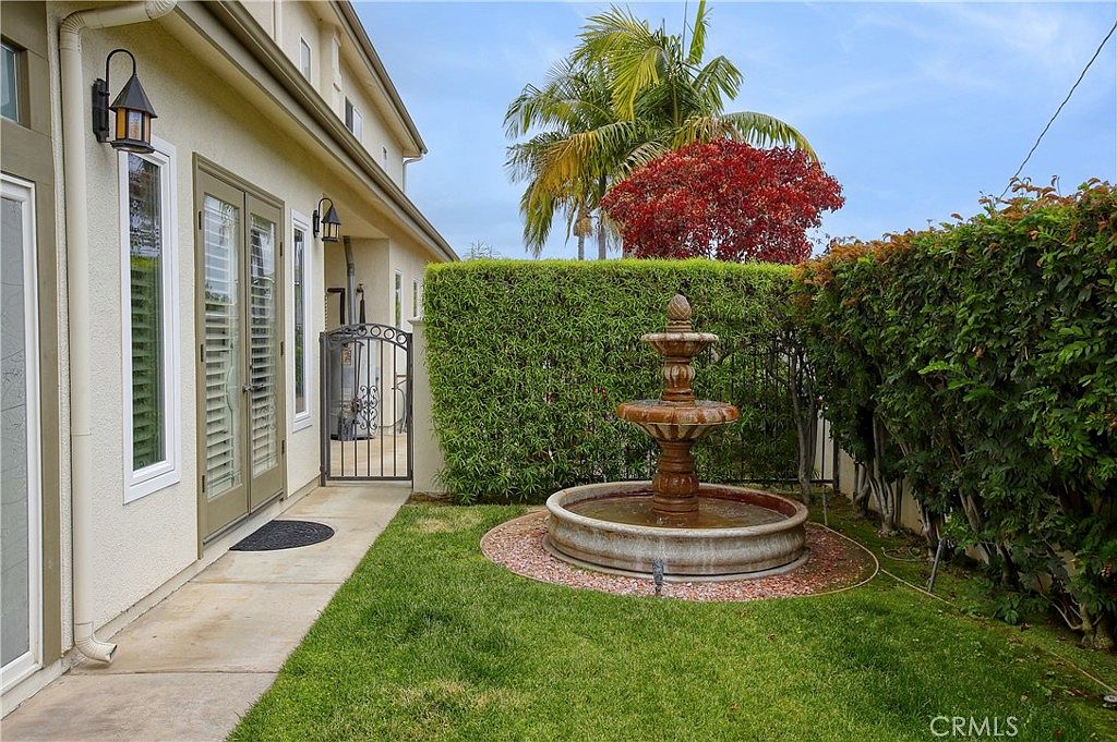 The side-yard fountain courtyard with a three-tier fountain, hedge wall, and Italian-iron gate
