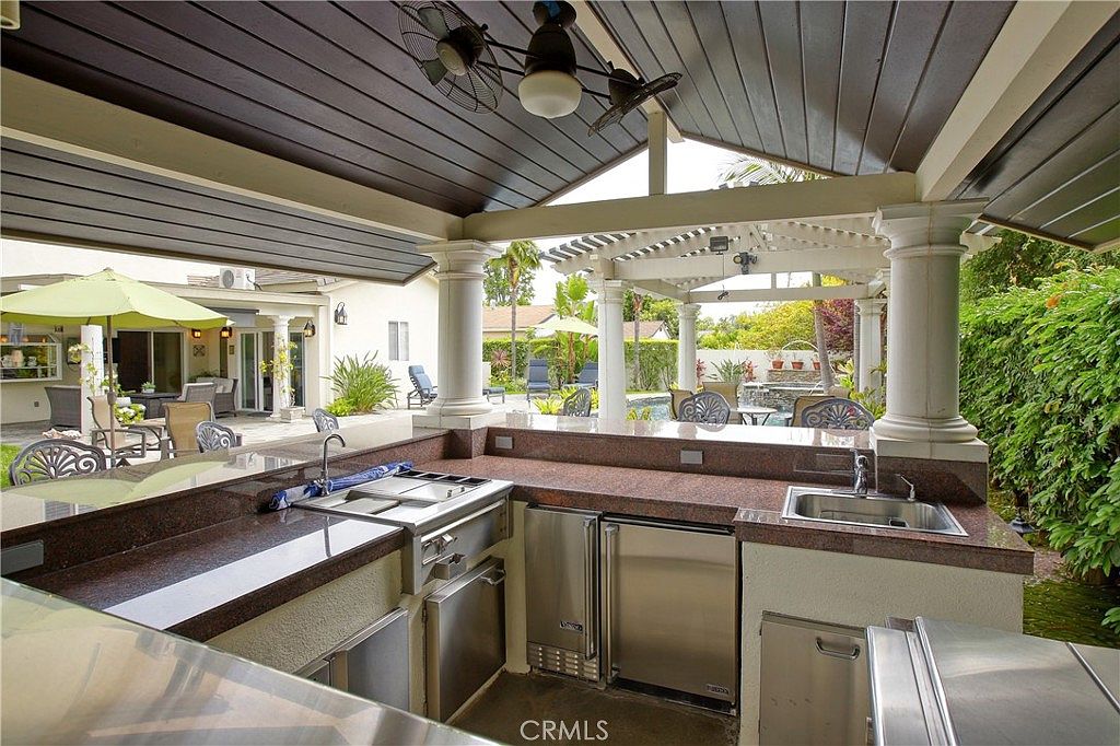 The covered outdoor kitchen with granite counters, stainless appliances, and pergola roof