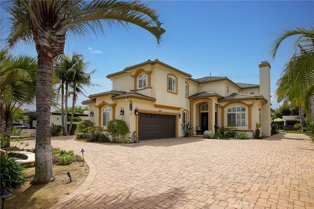 An alternate exterior angle of the residence framed by mature palms and a paver drive